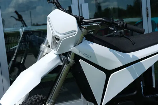 Side profile of a white Volt Surge V electric dirt bike showcased outdoors in Australia, featuring aggressive knobby tyres, inverted front forks, rear mono-shock suspension, and a compact battery/motor unit — ideal for Aussie trail riders seeking a quiet, zero-emission off-road bike