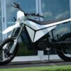 White Volt Surge V electric dirt bike parked on a paved path in Australia, side view showing knobby off-road tyres and minimalist electric motor design