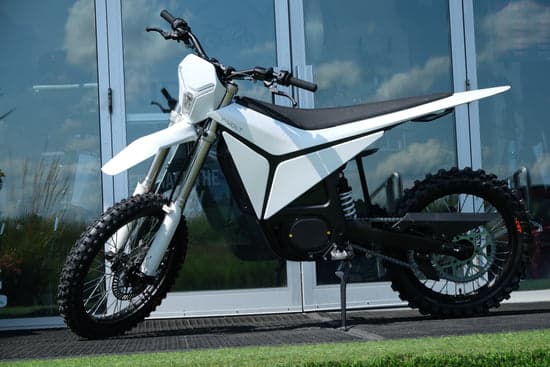 White Volt Surge V electric dirt bike parked on a paved path in Australia, side view showing knobby off-road tyres and minimalist electric motor design